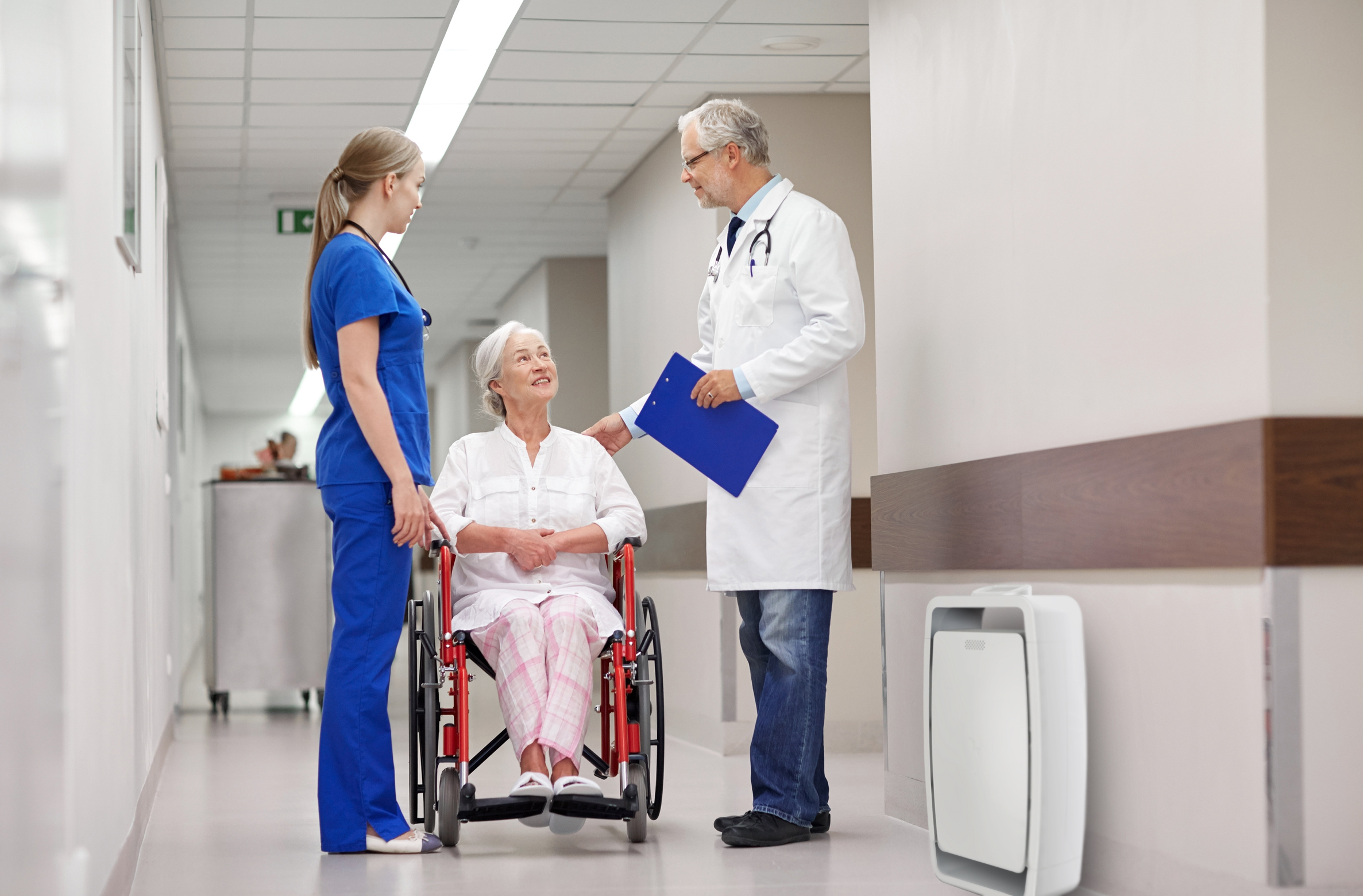 medicine, age, health care and people concept - doctor, nurse and senior woman patient in wheelchair at hospital corridor